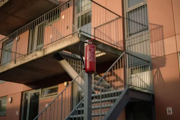 Nederlands appartementengebouw met brandtrap en rode brandblusser in middagzon, betonnen balkons met lange schaduwen.