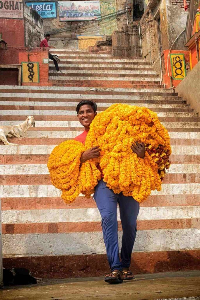 Shakti Bloemenmala Tonny Bol Indiase man onderaan trap India straatbeeld handen vol enorme hoeveelheid bloemenslingers
