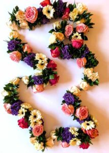 Shakti Bloemenmala Tonny Bol zachte warme sfeer ceremoniële bloemenkrans grote rozen anjers lisianthus gerbera's groene bladeren op maat gemaakt