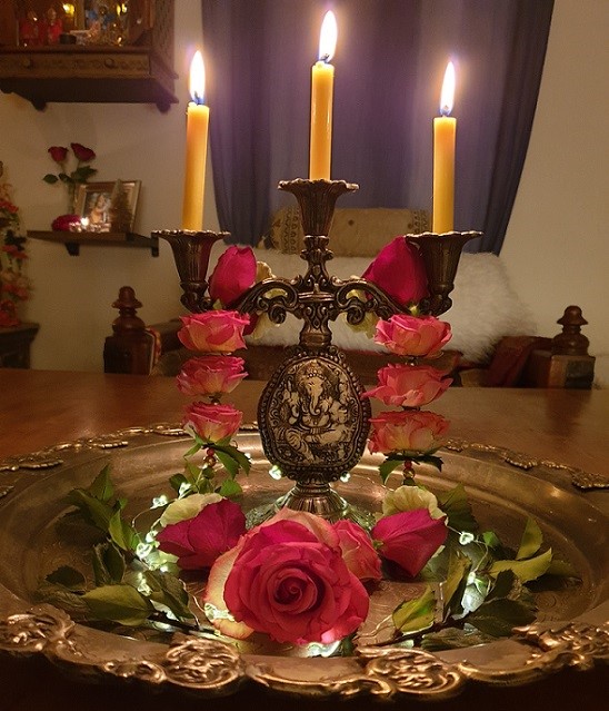 Shakti Bloemenmala, Tonny Bol, kandelaar met brandende kaarsen met rose bloemenslinger op sierlijke schaal