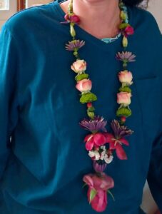 Shakti Bloemenmala Tonny Bol fleurige bloemenketting omgehangen donkerblauwe blouse geschenk verjaardag jubileum verwelkoming gast liefdevol eerbetoon