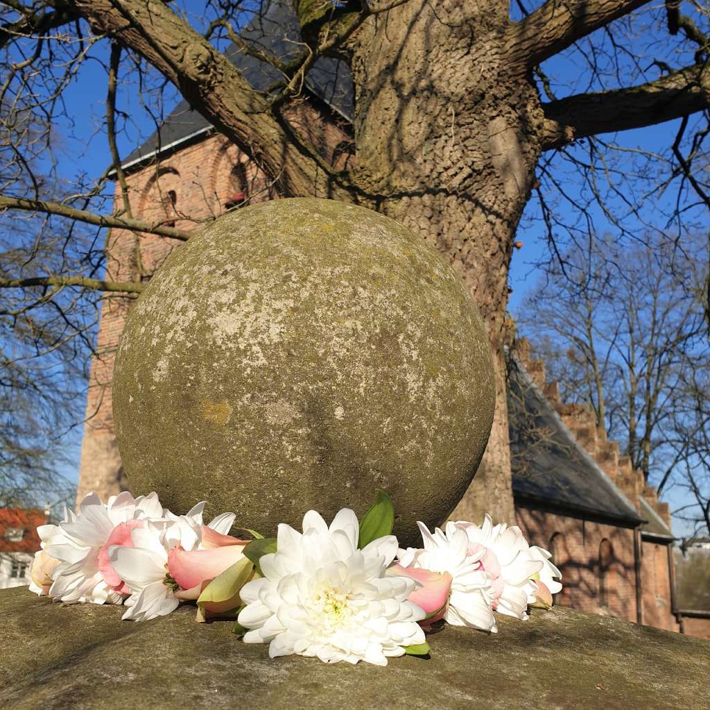 Shakti bloemenmala's Tonny Bol Mala om grote bol naast poort begraafplaats Beek-Ubbergen