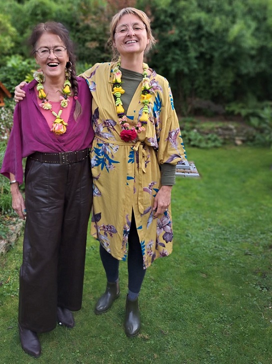 Shakti Bloemenmala, Tonny Bol, twee vrouwen met bloemenkransen om in tuin